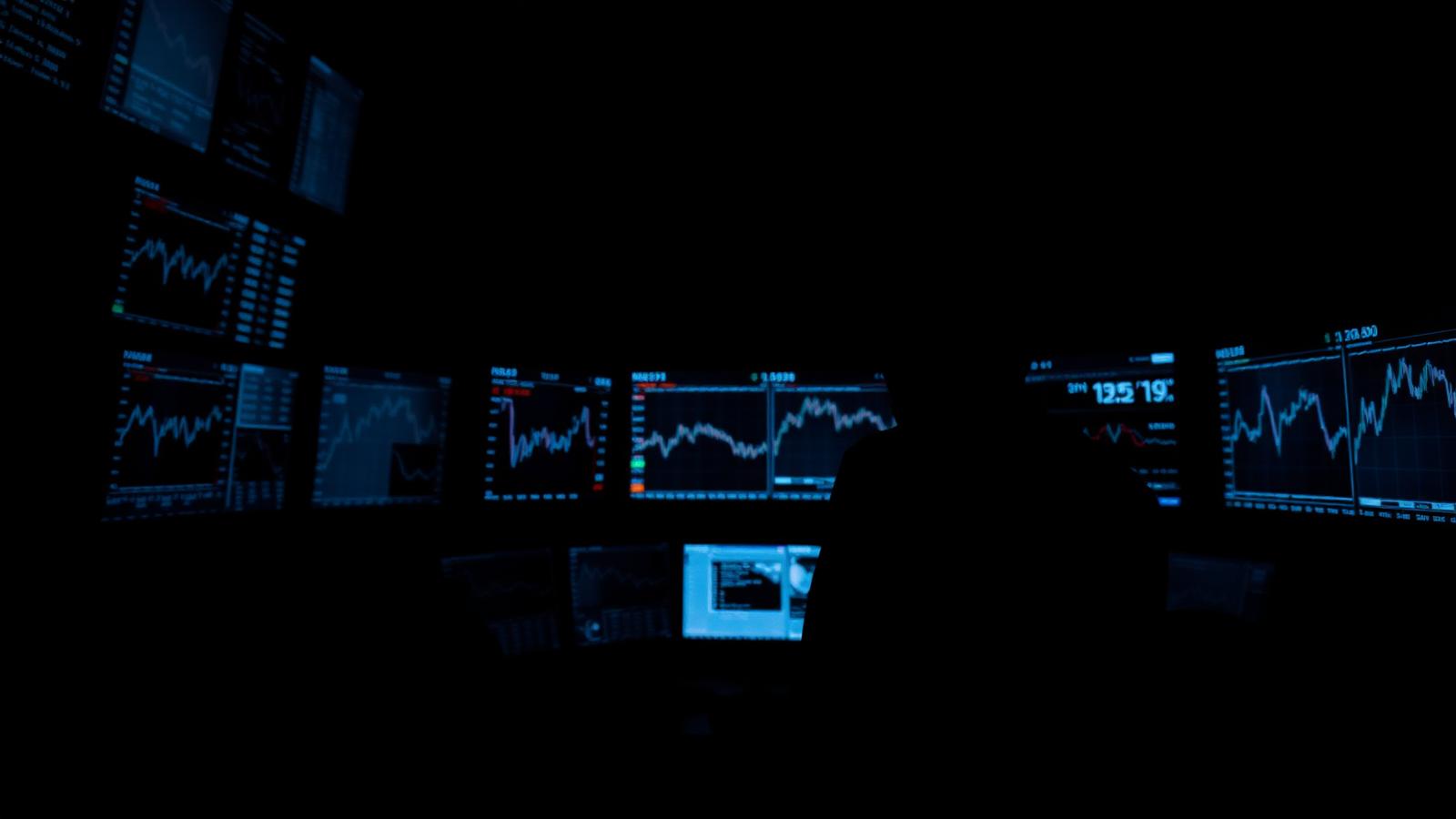 A lone trader silhouetted against a wall of dim market data screens